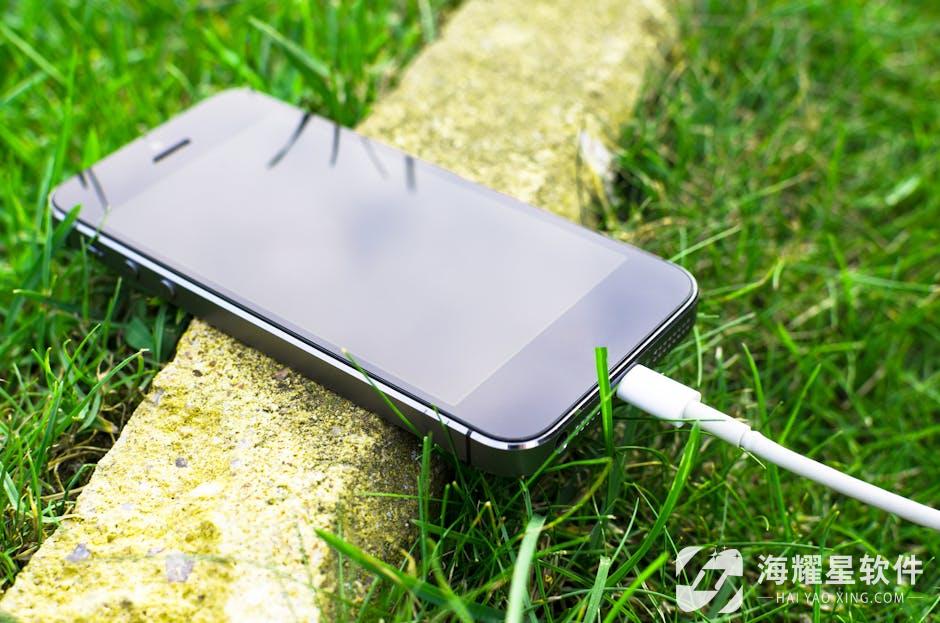 A smartphone with a charging cable rests on grass outdoors, showcasing modern technology in nature.
