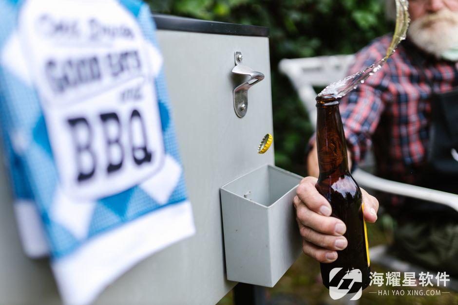 Close-up of a senior man opening a beer bottle at an outdoor barbecue gathering, splashing beer.