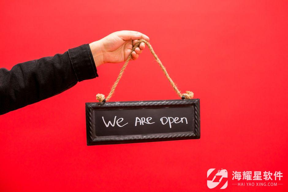 A hand holding a black sign with 'We Are Open' text, set against a vibrant red background.