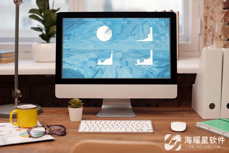 Stylish home office setup with desktop, plant, and eyeglasses on a wooden desk.